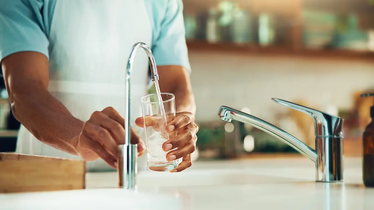 Filling a glass with tap water at home, showing the link between water quality and your health and safe drinking water practices.